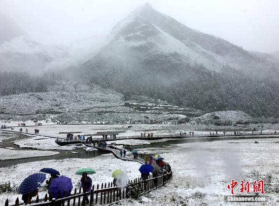 9月20日，受冷空氣影響，四川甘孜州稻城亞丁景區(qū)雪花飄舞，大霧彌漫，山峰披上白紗，銀裝素裹。正在景區(qū)內(nèi)游玩的海內(nèi)外游客紛紛用手機(jī)記錄雪景，并拍照留念。鐘欣 攝